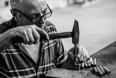 Un anciano artesano martilla metal con destreza en un taller, mostrando habilidad artesanal y precisión.