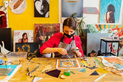 Artesana femenina enfocada creando vibrante arte en vidrio en un estudio colorido.